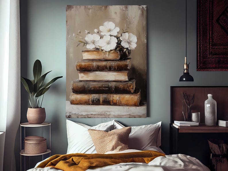 May include: An oil painting depicts a stack of aged books topped with a vase of white flowers. The books are brown and beige, with visible wear and tear. The artwork hangs above a bed with white pillows and a mustard-colored blanket. A potted plant sits on a side table.