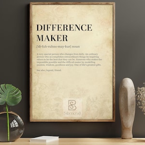 May include: A printable wall art print with a vintage aesthetic. The print features a definition of the word "Difference Maker" with a pronunciation guide and a description of the word's meaning. The print is framed in a brown wood frame and has a white background.