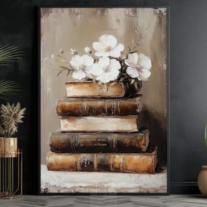 May include: An oil painting depicts a stack of old books with white flowers on top. The books are brown with gold lettering, and the background is a neutral beige. The artwork is framed in a black frame.