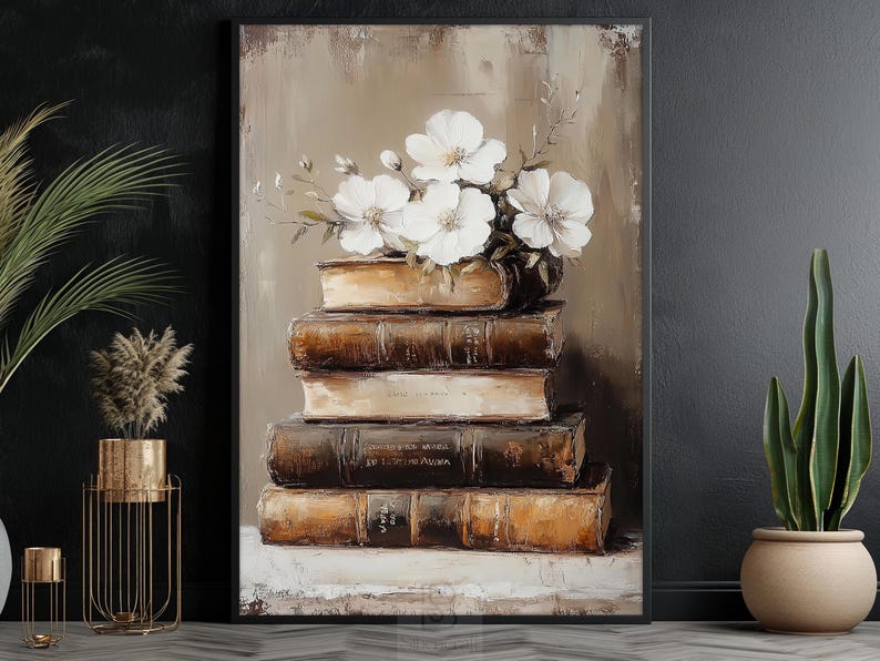 May include: An oil painting depicts a stack of old books with white flowers on top. The books are brown with gold lettering, and the background is a neutral beige. The artwork is framed in a black frame.