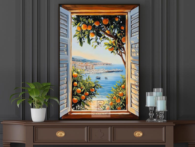 Op de afbeelding: Een ingelijst schilderij toont een kustlandschap door een open raam met blauwe luiken. Sinaasappelbomen omlijsten het uitzicht op de zee, boten en een verre stad. Het kunstwerk wordt tentoongesteld op een bruine kast.