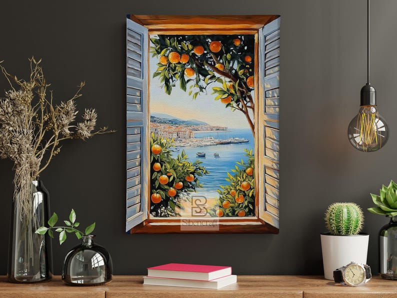 Op de afbeelding: Een ingelijst schilderij toont een kustlandschap door een raam met blauwe luiken. Sinaasappelbomen omlijsten het uitzicht op de zee, boten en een verre stad. Het schilderij wordt tentoongesteld op een houten oppervlak met decoratieve items.