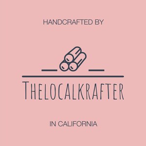 Puede incluir: Un logotipo sobre un fondo rosa. El logotipo presenta el texto "HANDCRAFTED BY" encima de un gr&aacute;fico de tres troncos. Debajo, el texto "THELOCALKRAFTER" y "IN CALIFORNIA". El logotipo es de color azul oscuro.