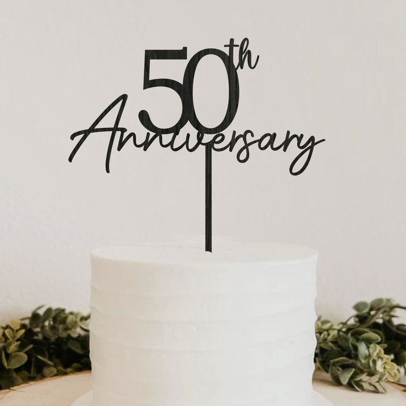 May include: Black acrylic cake topper with the text "50th Anniversary" in a cursive font. The number 50 is large and bold.
