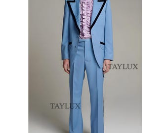 Pode incluir: Um fato azul claro com acabamentos pretos nas lapelas e bolsos. O fato inclui um casaco a condizer e calças de boca de sino. Uma camisa rosa com folhos é usada por baixo do casaco. A imagem inclui o texto "TAYLUX".