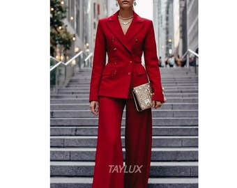 May include: A red double-breasted suit with wide-leg pants. The suit has gold buttons and is paired with a gold clutch. The image is taken outdoors on a set of stairs. The text "TAYLUX" is visible.