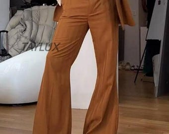 May include: A brown suit with flared trousers. The trousers have a high waist and a wide leg that flares out from the knee. The suit jacket is a matching brown colour. The image has the text "TAYLUX" in the lower left corner.