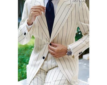 Può includere: Abito color crema con gessati neri, camicia bianca e cravatta blu navy. La giacca dell'abito ha bottoni neri e il marchio "TAYLUX" è visibile. Un orologio d'argento con quadrante nero è indossato al polso. L'abito è su misura.