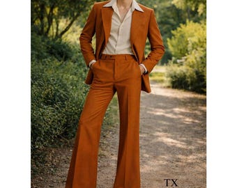 May include: A rust-colored suit with wide-leg pants, a matching blazer, and a cream-colored shirt. The suit is worn with sunglasses and tan shoes. The word "TAYLUX" is printed in white in the upper right corner and lower left corner of the image.