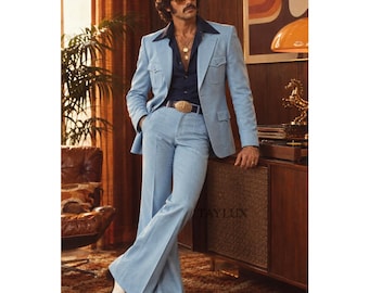 May include: A light blue suit featuring a blazer with two front pockets and wide-leg trousers, paired with a dark navy blue button-down shirt, a black belt with a large gold buckle, and white shoes. The text TAYLUX is visible in the image.