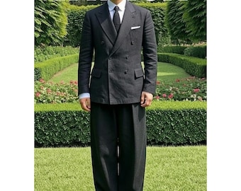 May include: A man in a dark gray double-breasted suit, white shirt, and black tie stands on a green lawn. The suit has a pocket square and is paired with matching wide-leg trousers. The word "TAYLUX" is at the top and bottom of the image.