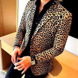 May include: A tan and black leopard print blazer. The jacket is worn over a black shirt. The image focuses on the blazer's distinctive pattern and the overall design of the garment, suitable for a smart casual look.