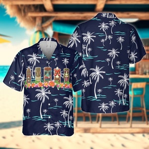 Könnte beinhalten: Ein blaues und weißes Hawaiihemd mit Palmenmuster und einer Reihe von Tiki-Figuren auf der Vorderseite. Das Hemd hat einen Knopfleisten vorne und kurze Ärmel.