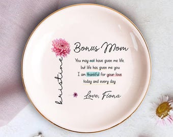 May include: A white ceramic trinket dish with a gold rim, featuring a pink floral design and the text "Bonus Mom." The dish includes a personalized message and the name "Kristine."