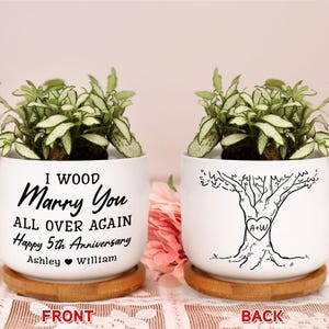 May include: Two white ceramic planters with green plants, each on a wooden coaster. One planter has the text "I WOOD Marry You ALL OVER AGAIN Happy 5th Anniversary Ashley William". The other has a tree design with "A+W" in a heart.