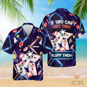 Puede incluir: Una camisa hawaiana azul y negra con temática de casino. La camisa presenta cartas de juego, fichas de póquer, dados y el texto "Si no puedes vencerlos, blúféalos".