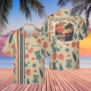 May include: A beige short-sleeved button-up shirt with a tropical print featuring palm trees, leaves, and disc golf discs. The shirt has a pocket on the left side with the text "Your Name" printed on it. The back of the shirt has a sunset scene with the text "Bangin' Chains".
