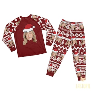 Könnte beinhalten: Ein passendes Pyjama-Set im festlichen Weihnachtsthema. Das langärmlige Oberteil und die Hose sind bordeauxfarben mit einem sich wiederholenden Muster aus einem Frauengesicht mit Weihnachtsmütze, Schneeflocken und anderen Weihnachtsdesigns. Das Oberteil hat eine große Gesichts-Grafik.