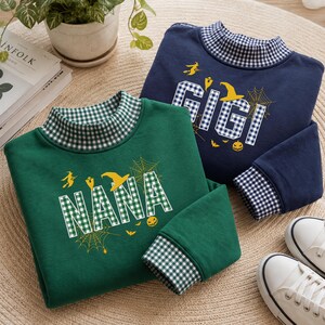 May include: A dark green sweatshirt with a mock neck and cuffs featuring a green and white gingham pattern, displaying the text NANA in gingham letters with yellow Halloween graphics. A navy blue sweatshirt with a matching blue gingham mock neck and cuffs, displaying the text GIGI in gingham letters with yellow Halloween graphics.