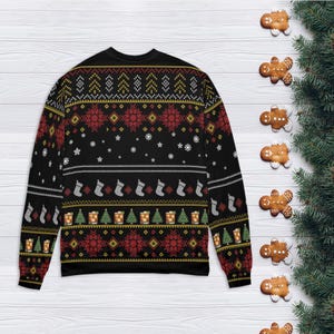 Op de afbeelding: Zwarte kersttrui met een feestelijk patroon. Het ontwerp bevat rode sneeuwvlokken, groene kerstbomen en witte kousen. De trui is versierd met gouden en witte accenten. Gemberkoekjes en dennentakken staan op de achtergrond.