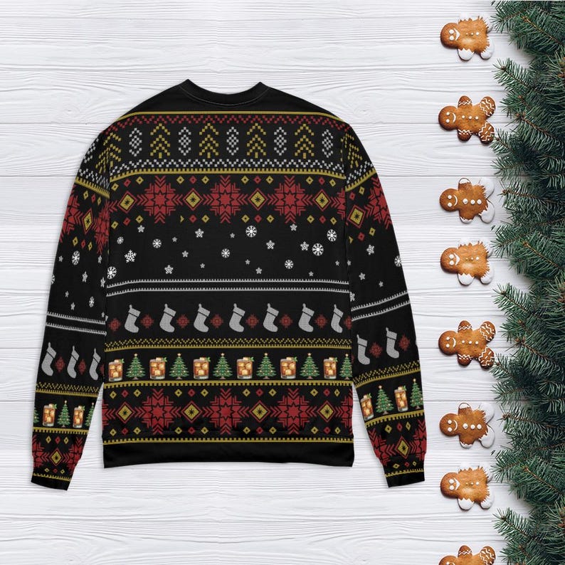 Op de afbeelding: Zwarte kersttrui met een feestelijk patroon. Het ontwerp bevat rode sneeuwvlokken, groene kerstbomen en witte kousen. De trui is versierd met gouden en witte accenten. Gemberkoekjes en dennentakken staan op de achtergrond.