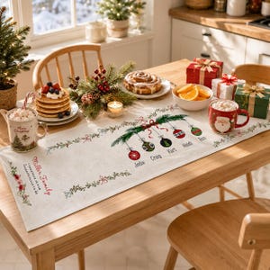 May include: A white fabric table runner featuring a printed Christmas design with hanging ornaments labeled with the names Jodie, Craig, Kurt, Heidi, and Ron, plus the text Miller Family, Together is our favorite place to be, and floral accents.