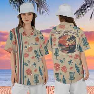 May include: A beige button-up shirt with a tropical print featuring palm trees, leaves, and disc golf discs. The back of the shirt has a sunset scene with a disc golfer and the text "Bangin' Chains". The front of the shirt has the text "Your Name".