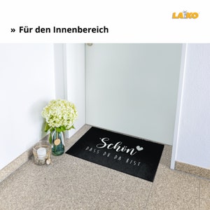 K&ouml;nnte beinhalten: Schwarze Willkommensmatte mit wei&szlig;em Text "Schon dass du da bist" und einem kleinen wei&szlig;en Herz.