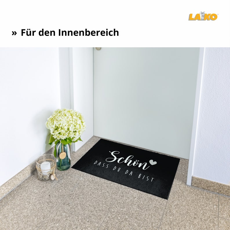 K&ouml;nnte beinhalten: Schwarze Willkommensmatte mit wei&szlig;em Text "Schon dass du da bist" und einem kleinen wei&szlig;en Herz.