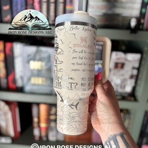 May include: A white stainless steel tumbler with a black and white graphic of a lighthouse and waves. The tumbler has a straw and a lid. The text "Enzo Bella Ladra" and "You're going to ruin me too" is printed on the tumbler.