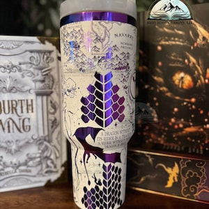 May include: A white stainless steel tumbler with a purple and white dragon design. The tumbler features a map of the fictional land of Andor from the Wheel of Time series. The text "A dragon without its rider is a tragedy. A rider without a dragon is even more so." is printed on the tumbler.