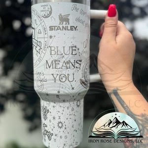 Può includere: Un bicchiere in acciaio inossidabile bianco con un design nero e argento che presenta costellazioni, segni zodiacali e il testo "The stars are about you" e "Blue means you". Il bicchiere ha un coperchio nero e un manico nero. Il nome del marchio "STANLEY" è stampato sul bicchiere.
