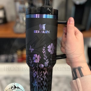 May include: Black Stanley tumbler with a handle and a straw. The tumbler features a floral design in purple and blue hues, with the Stanley logo. The text "IRON ROSE DESIGNS, LLC" is also visible.