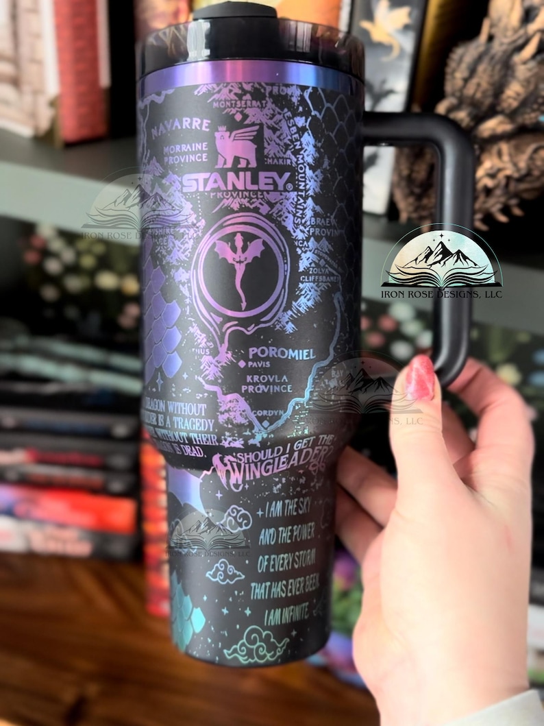 May include: A black stainless steel travel mug with a colorful iridescent finish. The mug features a map of the fictional world of the Wheel of Time book series, with text that reads "Should I get the Wingleader?" and "I am the sky and the power of every storm that has ever been. I am infinite."
