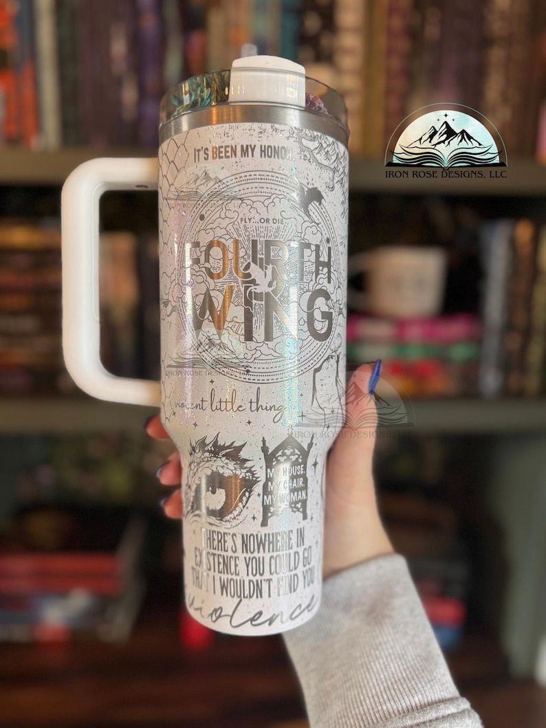 May include: A white stainless steel tumbler with a black and white graphic design featuring the text "Fourth Wing" and a quote from the book. The tumbler has a white handle and a black lid.