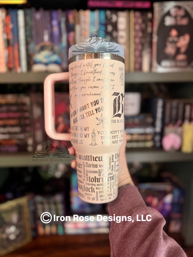 May include: A cream-colored tumbler with a light pink handle, featuring black text and graphics. The design includes quotes, a stylized "B", and the words "Matthew", "Darius", and "Kaylock". The tumbler has a silver lid with a mountain design.