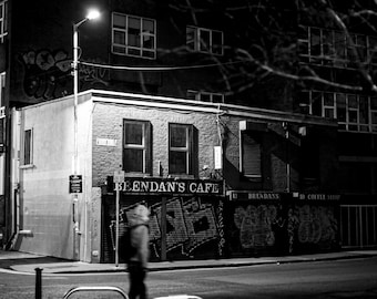 May include: A black and white photo of a cafe at night with the name "Brendan's Cafe" above the entrance. The cafe has graffiti on the walls and a sign that says "Brendan's" above the door.
