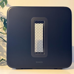 Könnte beinhalten: Ein schwarzer Sonos Wireless-Subwoofer mit einem sechseckigen Lautsprechergitter und dem Sonos-Logo auf der Vorderseite.