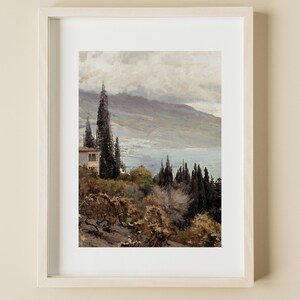 以下が含まれることがあります： 水辺と遠くの山々を望む風景画が額装されています。手前に濃い緑色の木々と小さな白い建物があります。