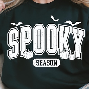 May include: Black sweatshirt with the words "SPOOKY SEASON" in white block letters. The design includes white bats and pumpkins, perfect for Halloween. A comfortable, casual top for the spooky season.