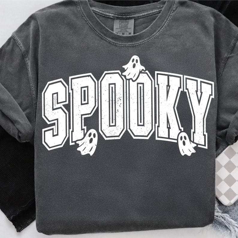 May include: Dark grey crew neck sweatshirt featuring the word "SPOOKY" in white, outlined block letters. Small white ghost graphics are placed around the word. The sweatshirt has a vintage, worn appearance.