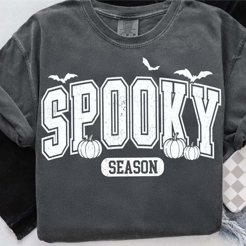 May include: Dark gray long-sleeve shirt with the words "SPOOKY SEASON" in white block letters. The design includes white bats and pumpkins. The shirt has a vintage, worn look.