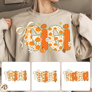 May include: Beige sweatshirt with a colorful fall-themed design. The word "GIGI" is displayed in large, orange letters filled with pumpkin and floral patterns. A bow and daisies accent the design, perfect for autumn.