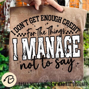 May include: A brown t-shirt featuring the quote "I DON'T GET ENOUGH CREDIT For The Things I MANAGE not to say." The text is in black and white, with star accents. The shirt is held up by a hand.