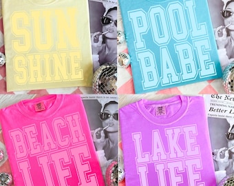 Puede incluir: Cuatro camisetas coloridas con texto temático de verano. Las camisetas son amarillas, azules, rosas y moradas. La camiseta amarilla dice "SUN SHINE", la camiseta azul dice "POOL BABE", la camiseta rosa dice "BEACH LIFE" y la camiseta morada dice "LAKE LIFE".