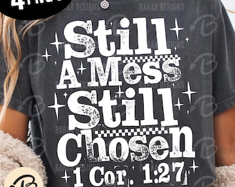 Może przedstawiać: Ciemnoszara koszulka z białym napisem "Still A Mess Still Chosen" oraz cytatem z Biblii "1 Kor. 1:27." Projekt ma postarzany, vintage wygląd z gwiazdkami.
