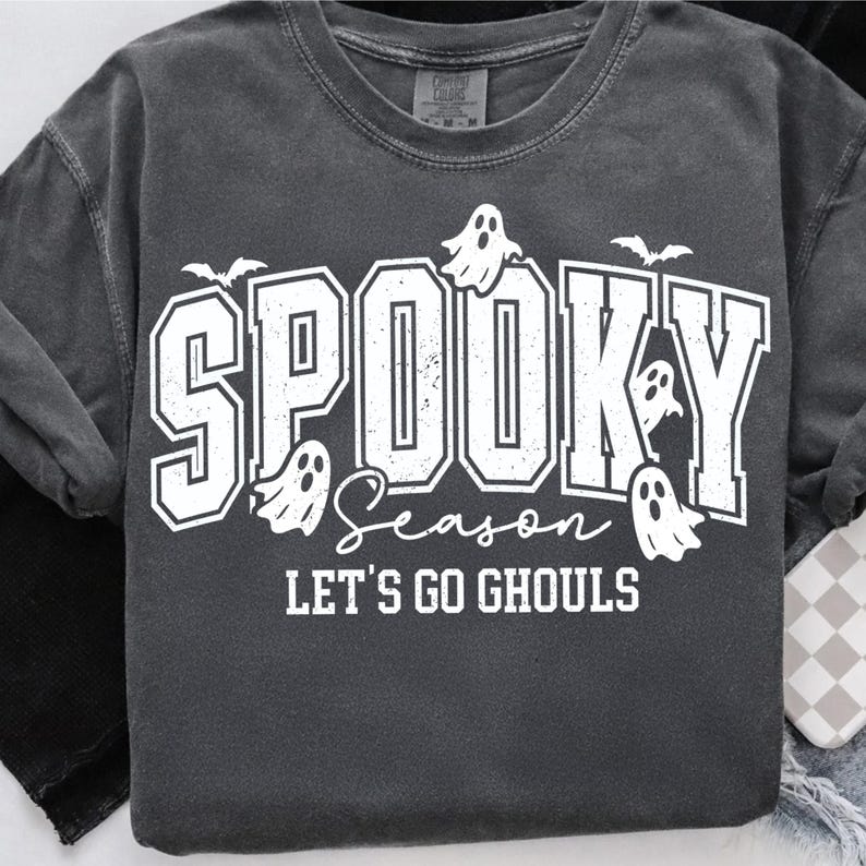 May include: Dark gray t-shirt with the words "Spooky Season" in a white, bold font, along with ghost and bat graphics. The phrase "Let's Go Ghouls" is also printed on the shirt, perfect for Halloween.