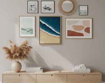 May include: A collection of framed art and decor, including landscape paintings, abstract art, and a round woven mirror. A wooden console table holds a vase with dried pampas grass and decorative books. The color palette is neutral with natural tones.