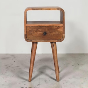 May include: A wooden nightstand with a drawer and open shelf. The nightstand has a warm brown finish, rounded edges, and three angled legs. The drawer features a dark knob. The nightstand is approximately 24 inches tall.