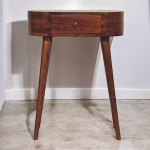 May include: A dark brown wooden side table with a single drawer and rounded oval top. The table has three legs and a minimalist design.